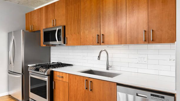 A kitchen detail with wood cabinets, white subway tile backsplash, stainless steel faucet and appliances, and white countertop.